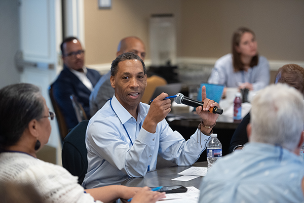 Scott Wilkes speaks into a microphone. He's in a conference room surrounded by other social work leaders